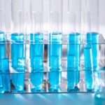 Rack of glass test tubes filled with blue liquid beside a laboratory flask