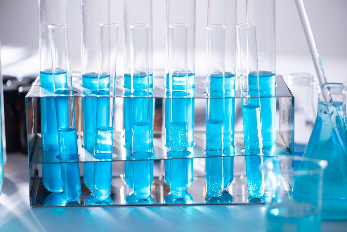 Rack of glass test tubes filled with blue liquid beside a laboratory flask